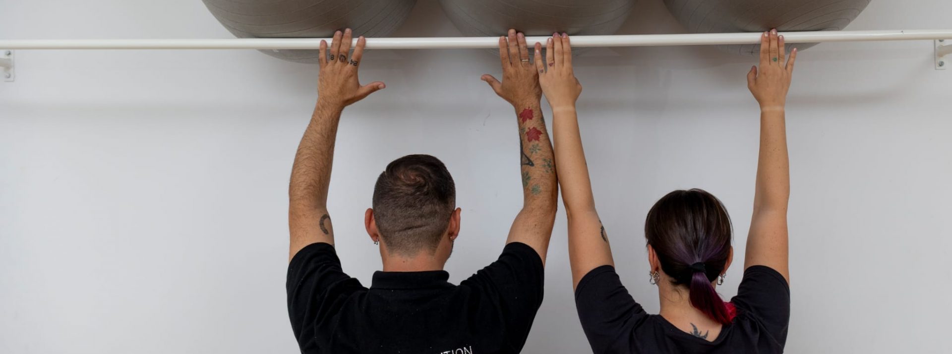 Dos personas sujetando una barra sujeta a la pared con tres fitballs